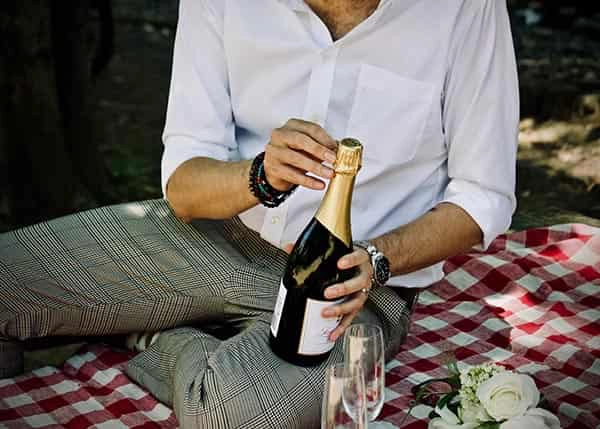 hombre abriendo botella de champagne picnic